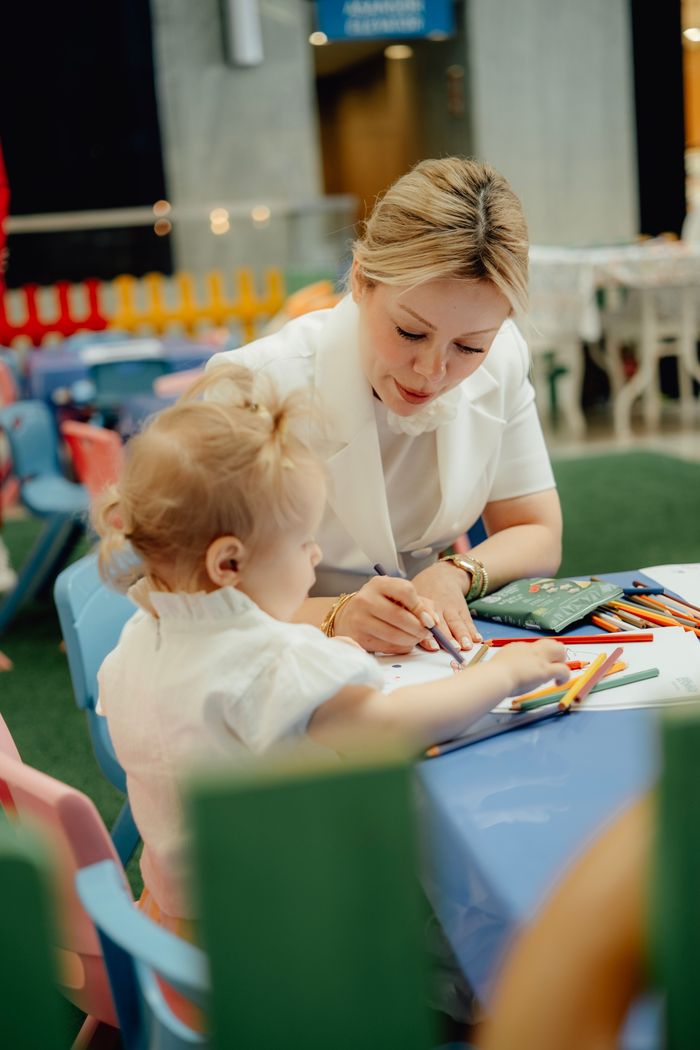 A loving mother helps her child draw at a colorful kindergarten setting.