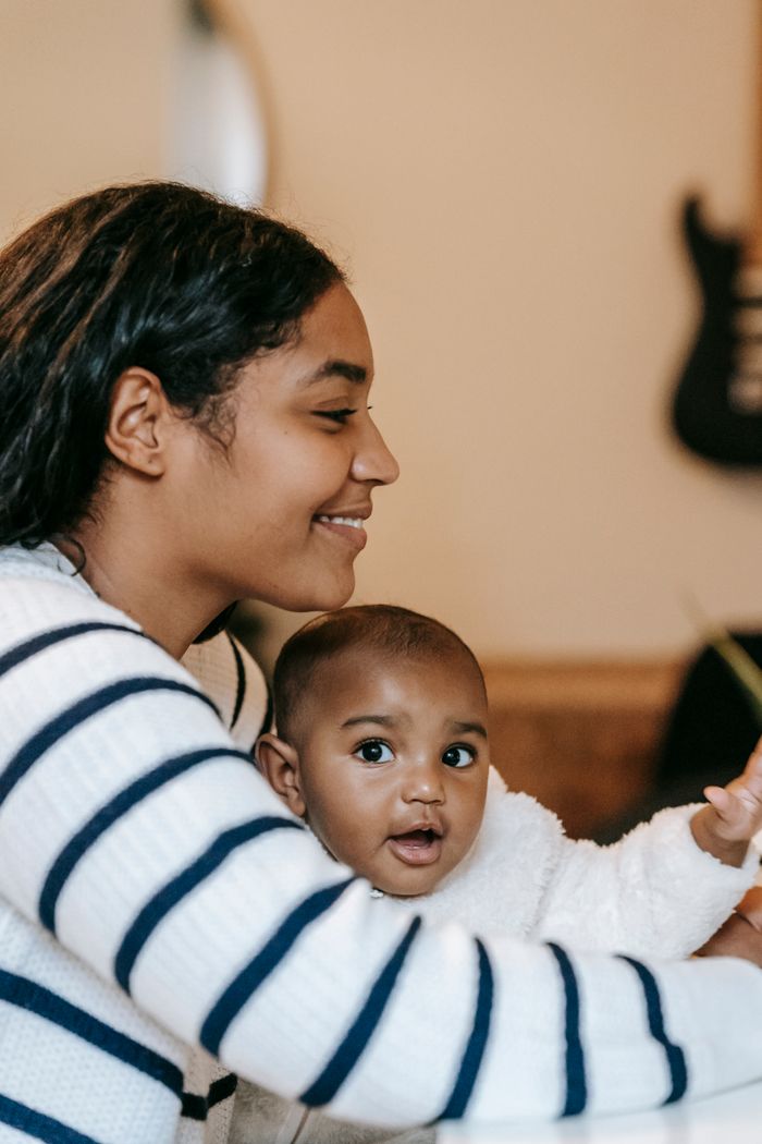 Happy ethnic mother and child in casual outfit spending time near table at bright home
