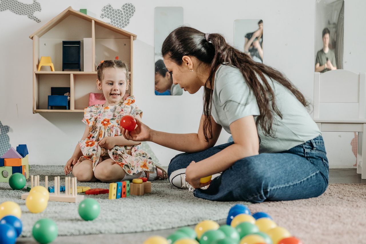 A young girl and woman engaging in an educational play session in a cozy preschool setting.